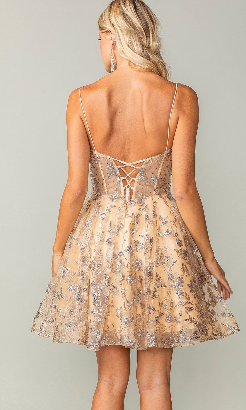 A woman stands with her back to the camera wearing the Short Glitter-Print Homecoming Dress 3343, a budget-friendly, short, sleeveless gold dress featuring silver floral patterns and a lace-up back detail.
